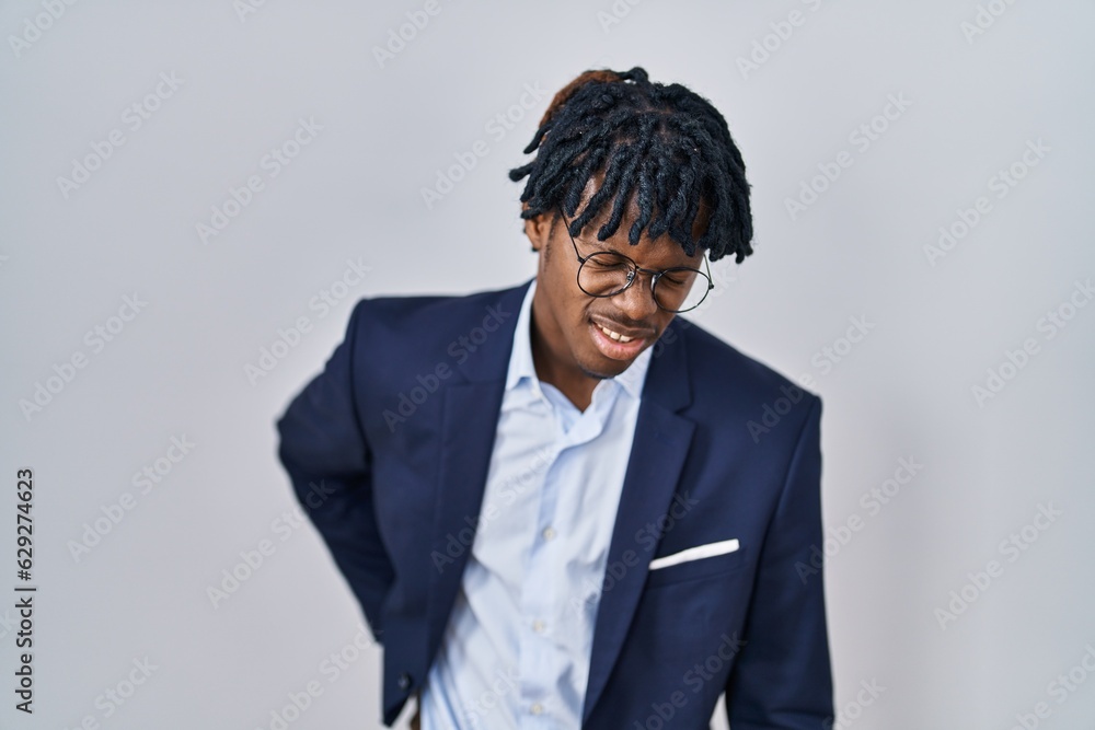 Young african man with dreadlocks wearing business jacket over white background suffering of backache, touching back with hand, muscular pain Young african man with dreadlocks wearing business jacket over white background suffering of backache, touching back with hand, muscular pain
