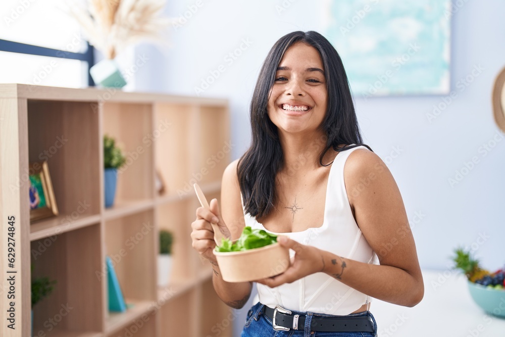 Brunette woman eating a salad at home celebrating crazy and amazed for success with open eyes screaming excited. Brunette woman eating a salad at home celebrating crazy and amazed for success with open eyes screaming excited.