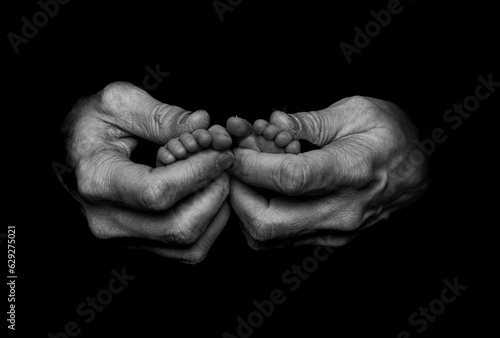 Wrinkled hands holding the feet of a newborn in grayscale