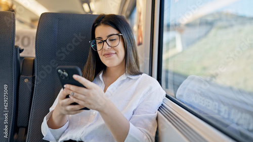 Young beautiful hispanic woman smiling using smartphone sitting inside train wagon