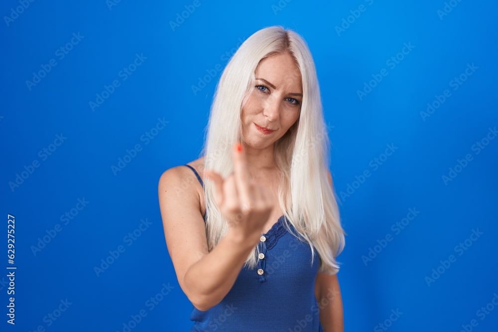 Caucasian woman standing over blue background showing middle finger, impolite and rude fuck off expression Caucasian woman standing over blue background showing middle finger, impolite and rude fuck off expression