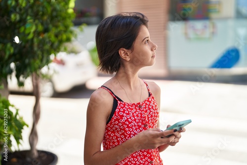 Adorable hispanic girl using smartphone with serious expression at street