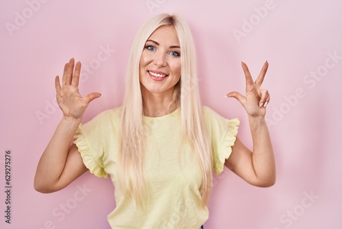 Caucasian woman standing over pink background showing and pointing up with fingers number eight while smiling confident and happy.