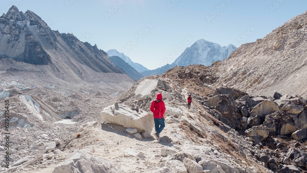 two people walking up a narrow dirt path between mountains with rocks