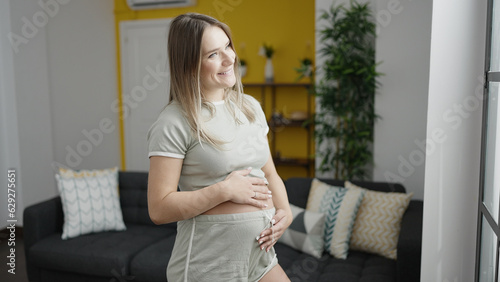 Young pregnant woman smiling confident touching belly at home