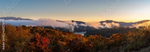 Scenic panoramic landscape featuring mountains cloaked in a mystical fog, with lush autumnal forest © Azeller/Wirestock Creators