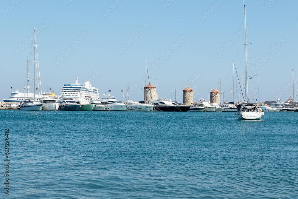 selective focus on Mandraki harbor with passenger boats and old windmills near Fort Saint Nicholas