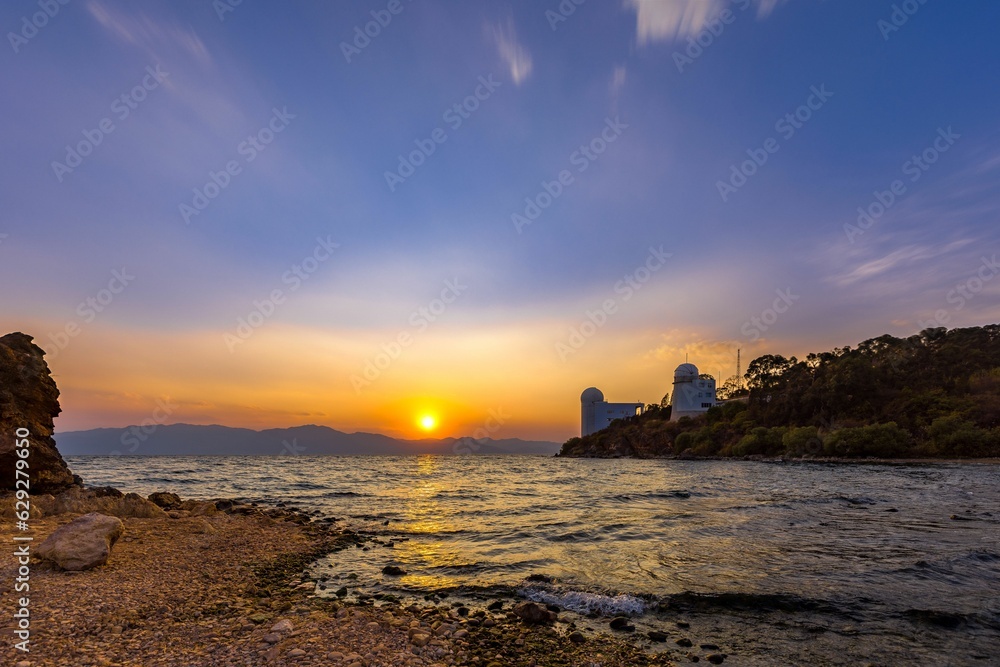 Serene bright orange sunset over the calm sea with a rocky shore