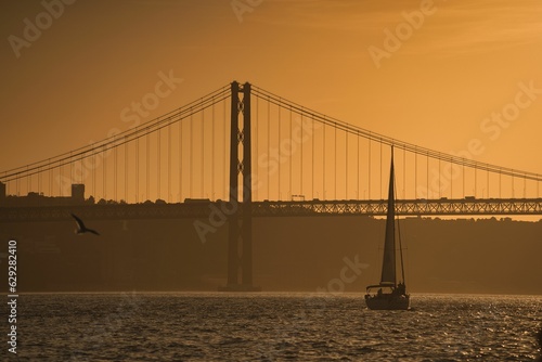 Stunning sunset view of Lisbon, Portugal, with a sailboat sailing across a bridge