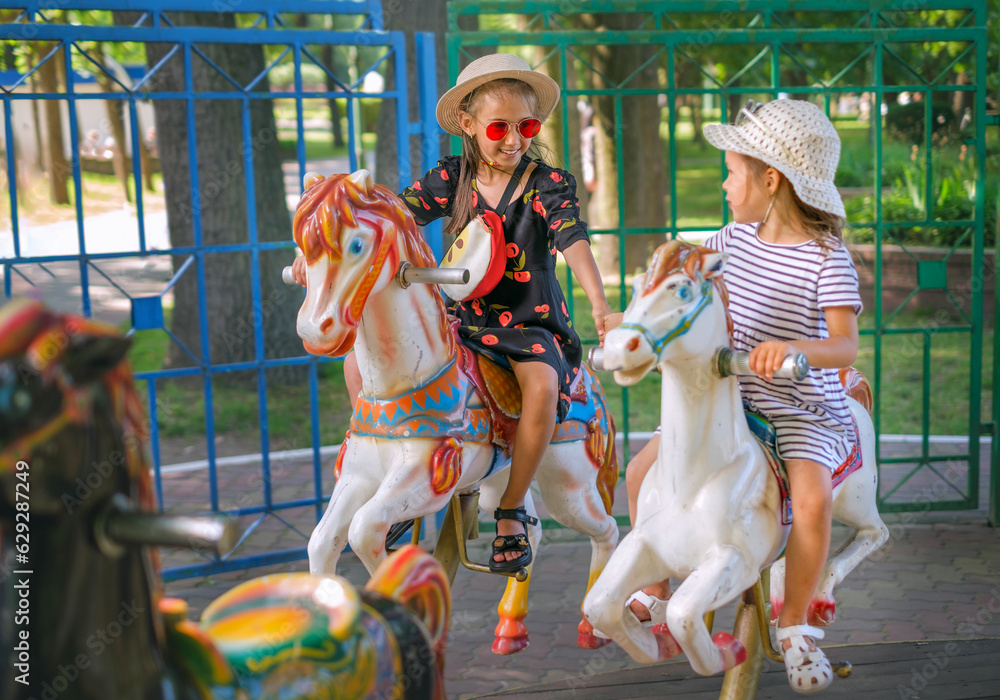 The sisters ride in a circle on a carousel sitting on colored horses. Kids have fun at the amusement park