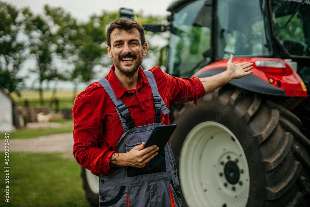 Portrait of a farmer man using a digital tablet and standing next to the tractor. Modern agriculture concept
