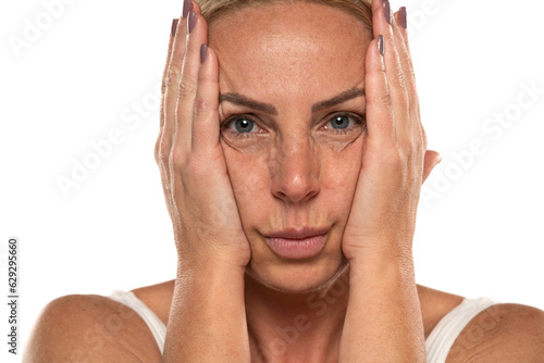 Middle aged blond woman squeezes her face skin with her hands on a white background