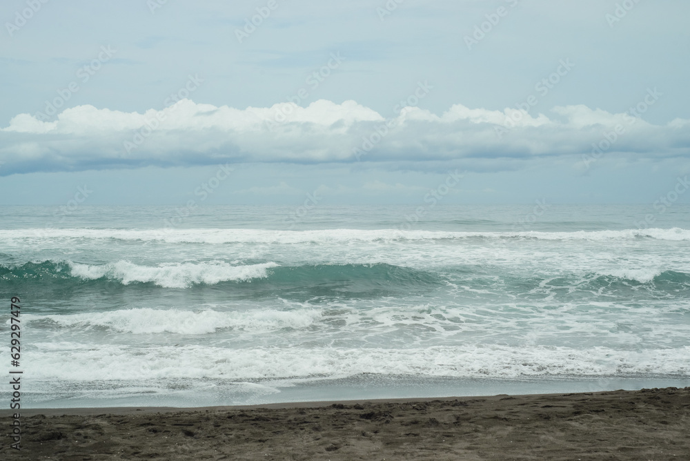 Landscape of a beach on the Mexican Pacific coast. Sea with many waves and cloudy sky.