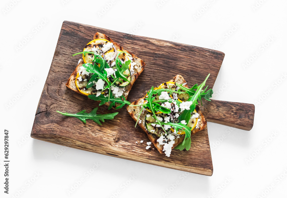 Φωτογραφία Grilled zucchini, arugula, feta cheese toast on a wooden chopping board, top vie
