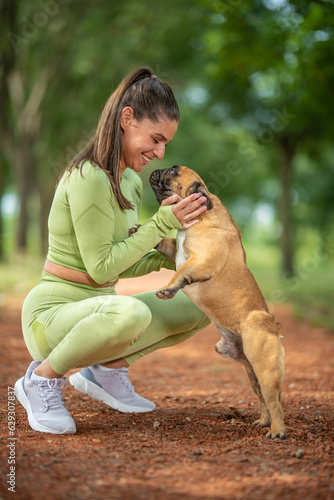 a girl plays with a french bulldog in the park on a jogging track