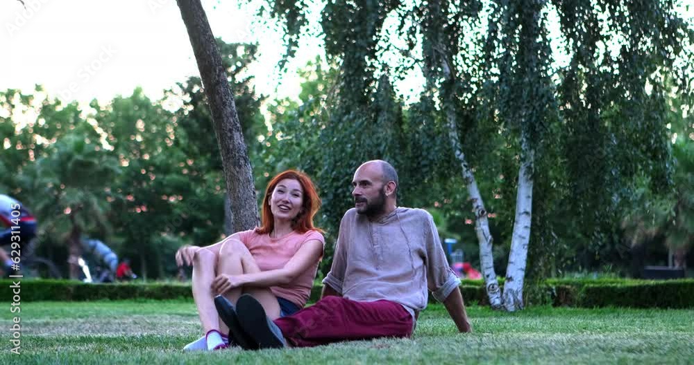 The couple sits on the grass in the park, engaging in a delightful conversation, sharing laughter, and cherishing beautiful moments together The couple sits on the grass in the park, engaging in a delightful conversation, sharing laughter, and cherishing beautiful moments together
