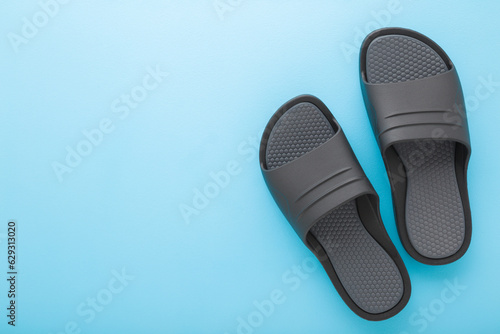 Dark gray black foam slippers on light blue table background. Pastel color. Closeup. Male summer footwear. Empty place for text. Top down view.