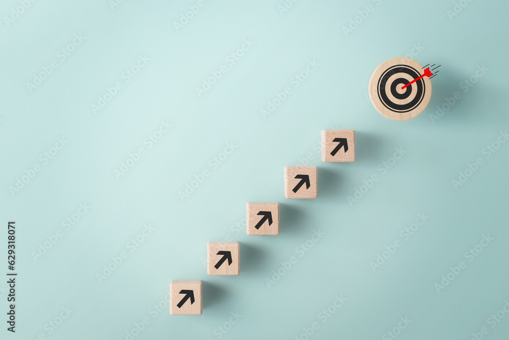 Business growth, objective goal achievement concept. Wooden block with target aiming dart board and arrow up on blue background top view