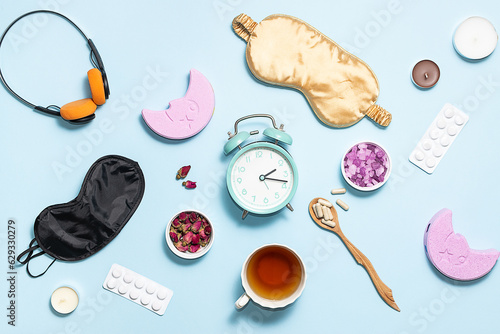 Insomnia concept. Alarm clock, sleeping mask, herbal tea, aromatic salt and natural pills on light blue background top view. 