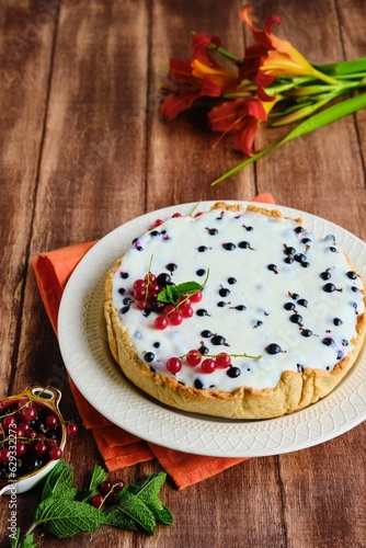 Dessert, a whole round cheesecake with blackcurrant on shortcrust pastry on a ceramic plate on a wooden background. Summer desserts, pastries with berries.