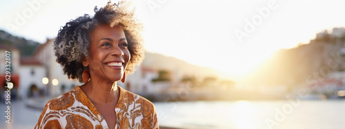 Lifestyle portrait of happy mature black woman with curly gray hair walking along idyllic waterfront boardwalk