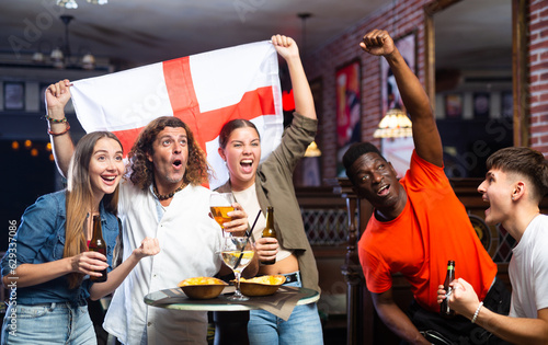 Group of England football team fans spending time in bar, drinking bear and having fun. People with state flag in pub.