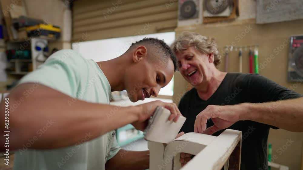 Experienced Carpenter and Young Apprentice Engaged in Polishing Wood at Local Carpentry Workshop. Master carpenter guiding employee at work Experienced Carpenter and Young Apprentice Engaged in Polishing Wood at Local Carpentry Workshop. Master carpenter guiding employee at work