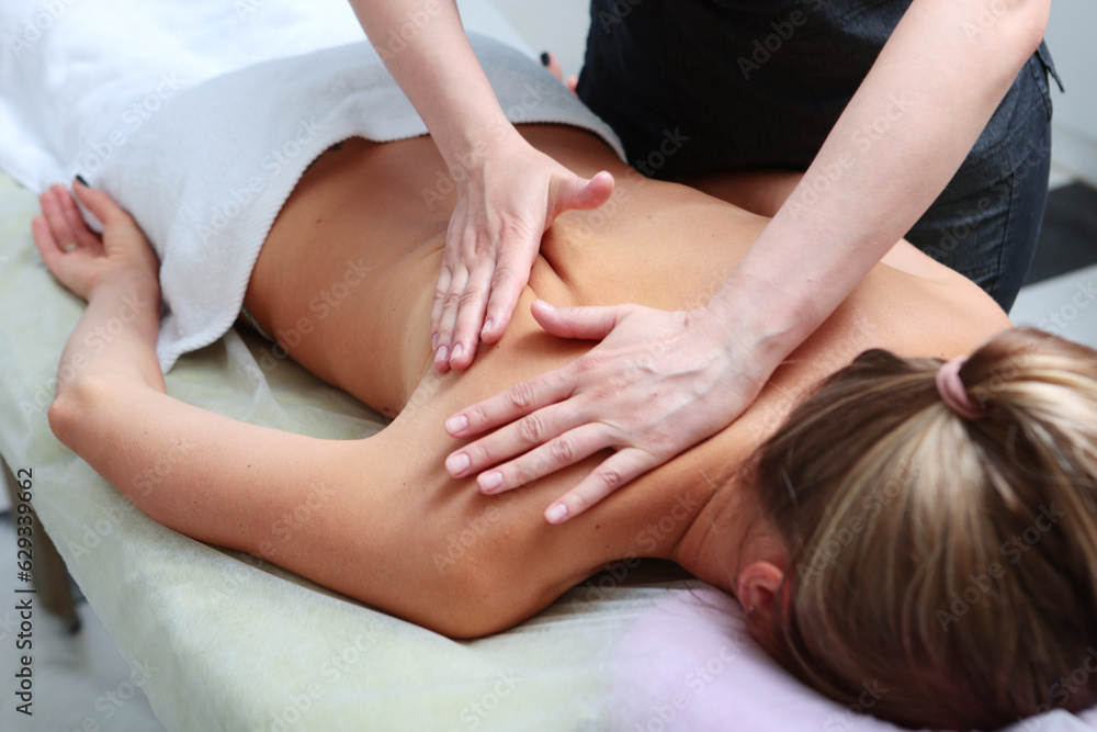 Masseur massages back and shoulder blades of young woman lying on massage table on light background. Unrecognizable personalities.Concept of massage spa treatments. Masseur massages back and shoulder blades of young woman lying on massage table on light background. Unrecognizable personalities.Concept of massage spa treatments.