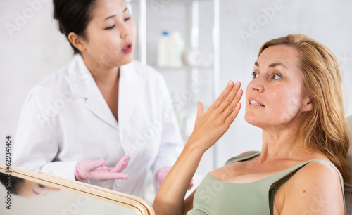 Blonde european women listening to professional medicine worker about facial beauty procedure