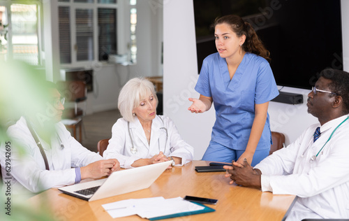 Young physician engaged in discussion with skilled doctors sitting around the table
