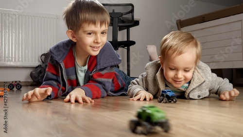 Baby boy with older brother having toy car race on floor. Children playing alone, development and education, games at home.