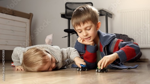 Two brothers lying on floor and playing with colorful toy cars. Children playing alone, development and education, games at home.