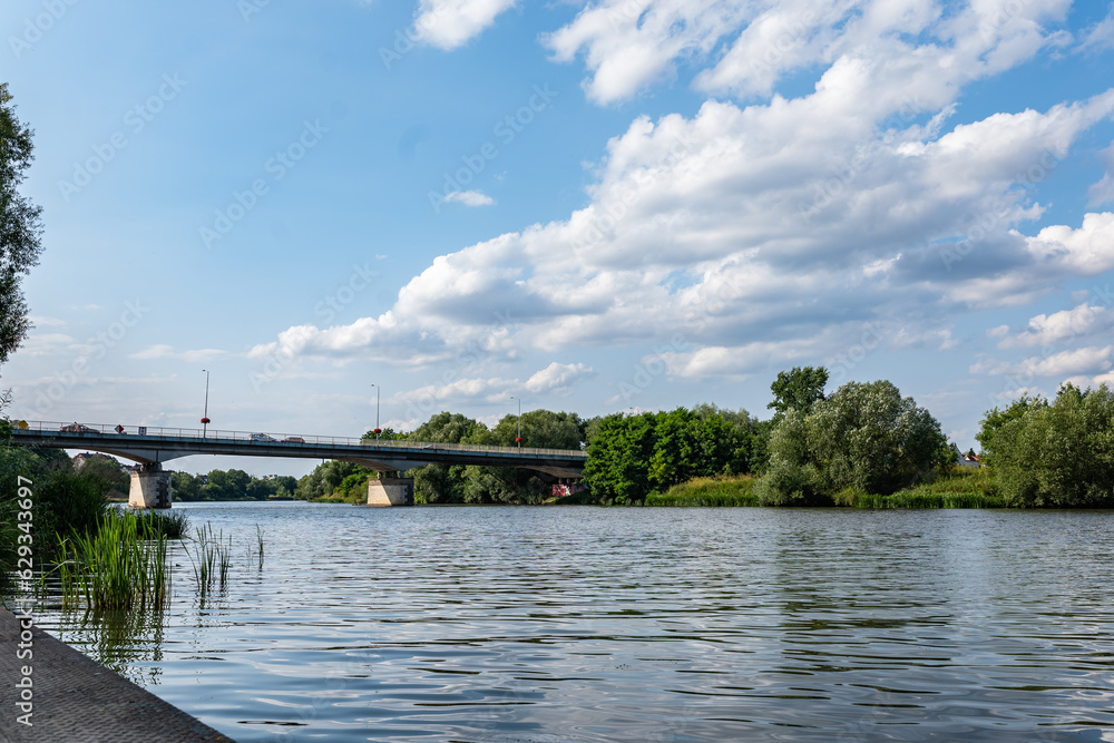 Rzeka Odra, w tle most lekko pochmurna pogoda, błękit nieba zieleń przy brzegu, pora letnia, Odra w odcinku województwa Opolskiego
