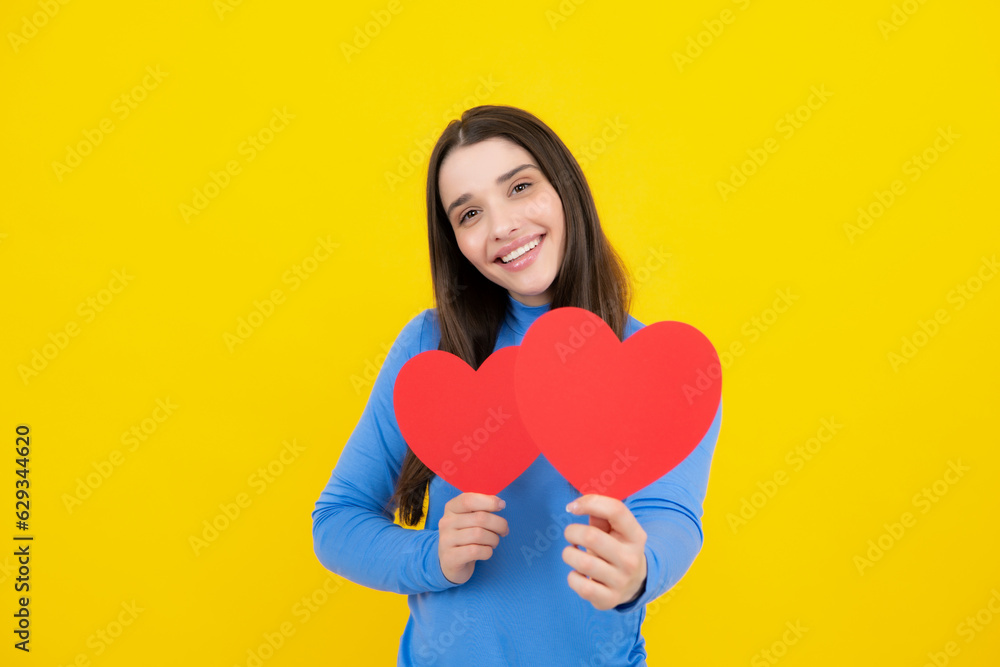 Portrait of lovely sweet cute pretty girl hold red paper card heart isolated over yellow background. Beautiful girl holding heart, love shape. Portrait of lovely sweet cute pretty girl hold red paper card heart isolated over yellow background. Beautiful girl holding heart, love shape.