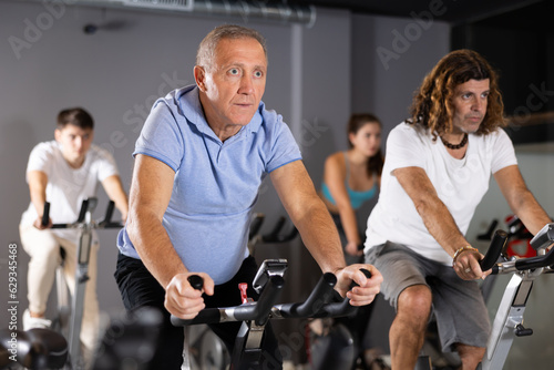 Focused aged man leading healthy active lifestyle doing cardio workout on exercise bike in gym