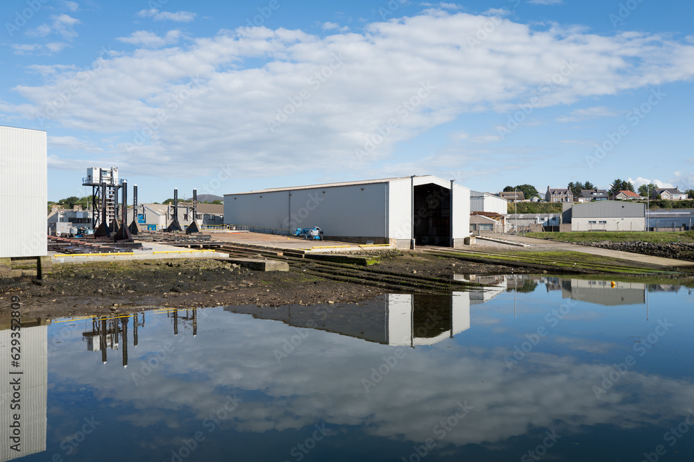 Obraz premium 30 July 2023. Buckie,Moray,Scotland. This is the site of Buckie Shipyard being reflected on very calm harbour water on a sunny day.
