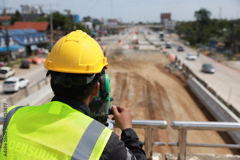 Civil or survey technician working at a new road construction site with a walkie-talkie and survey camera. Civil or survey technician working at a new road construction site with a walkie-talkie and survey camera.