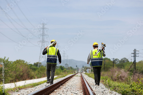 two surveyors hold the tripod of a geography camera on the railway photo