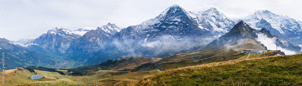 Wide panorama of Grindelwald valley and Swiss Alps. Mountain range of peaks Eiger, Wetterhorn, Schreckhorn, Monch, Jungfraujoch and Jungfrau from Mannlichen near Wengen and Lauterbrunnen, Switzerland