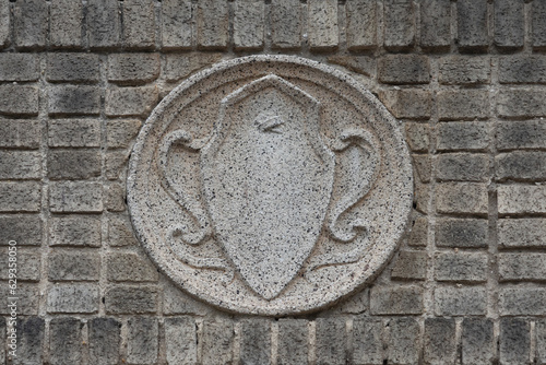 a molded concrete medallion in the art noveau style in neutral beige tones inset on a wall of beige gray bricks photo
