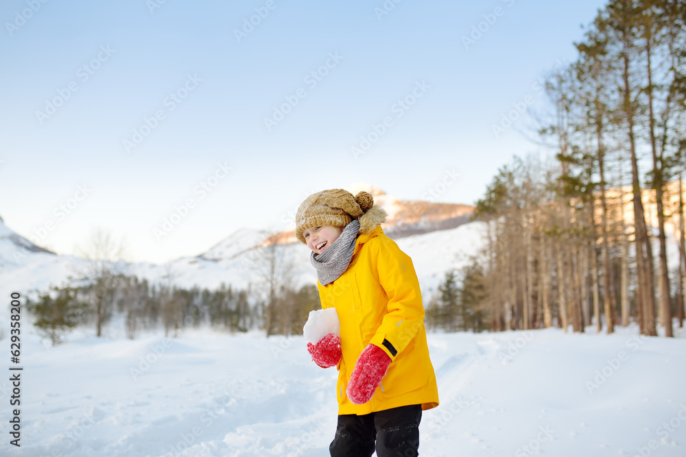 Preteen boy having fun playing with ice or snowball in forest among mountain valley on sunny day. Active winter outdoors leisure for family with kids. Travel in Lovcen National park