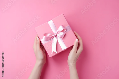 Female hands holding pink giftbox on the pink background, top view. Generative AI © lanych