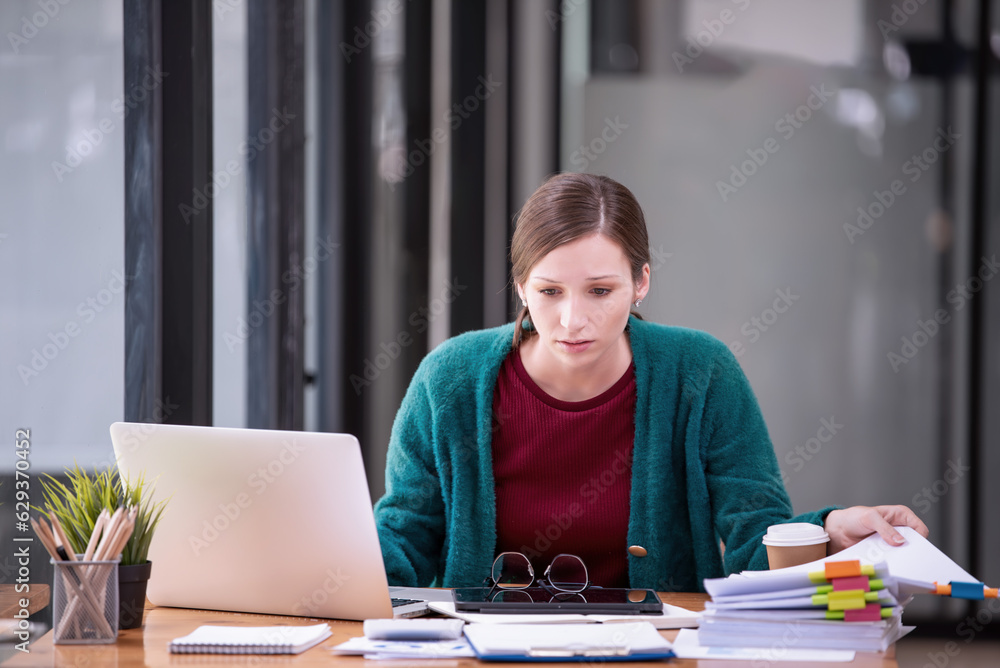 Businesswomen are stressed with work in front of a laptop and paper documents in the office. Businesswomen are stressed with work in front of a laptop and paper documents in the office.