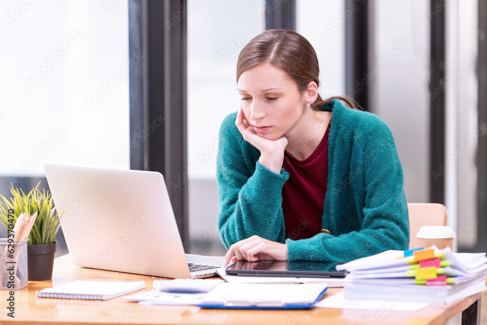Businesswomen are stressed with work in front of a laptop and paper documents in the office. Businesswomen are stressed with work in front of a laptop and paper documents in the office.