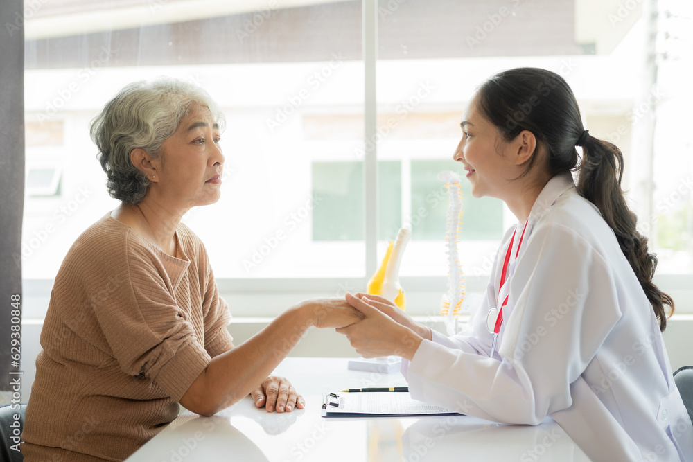 Family doctor examining smiling asian old woman using stethoscope at hospital An old woman talks and consults with a doctor about osteopathy. Health and wellness concept