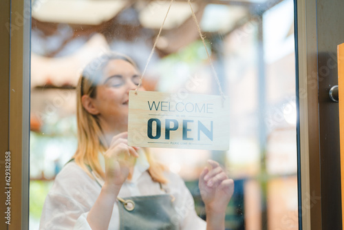 Hand of coffee shop staff woman wearing apron turning open sign board on glass door in modern cafe, morning of hotel service or restaurant retail store, small business owner in food and drink concept