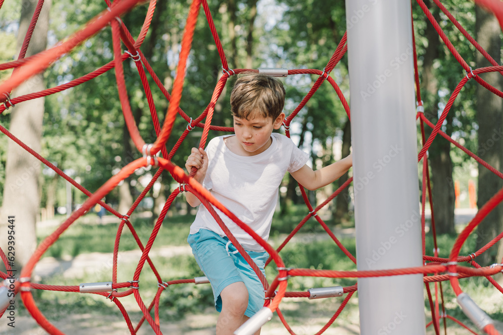 Happy boy child playing in rope spider web at playground. Children's sports. Happy boy child playing in rope spider web at playground. Children's sports.