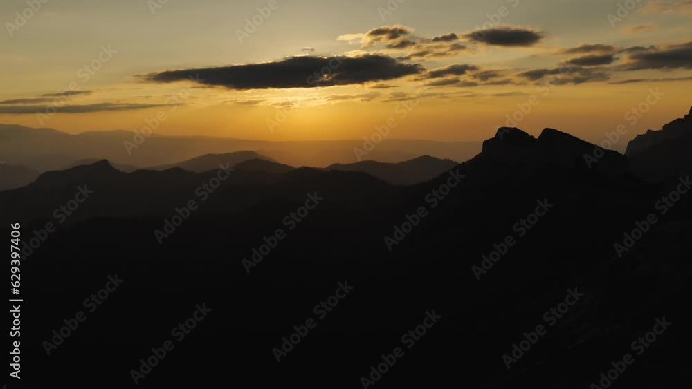 Yellow twilight in the mountains during sunset. The sun is hidden in the clouds. Long black rows of silhouettes of mountain peaks. Smooth recoil. Epic sunset in the mountains Yellow twilight in the mountains during sunset. The sun is hidden in the clouds. Long black rows of silhouettes of mountain peaks. Smooth recoil. Epic sunset in the mountains