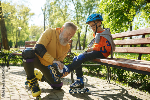 Father helping son to put on roller skates in urban park photo