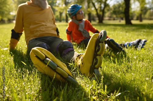 Happy man and boy rollerskaters rest on grass filed in park photo